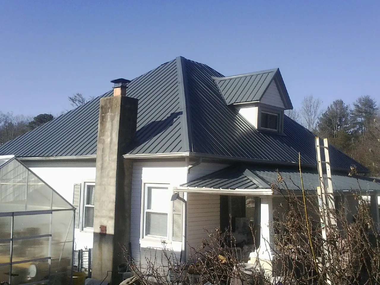 Dark blue standing seam metal roof on a white farmhouse with dormer — Slate & Tile Roof Repair by Roofing Brothers in Las Cruces