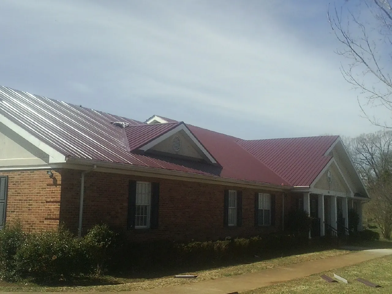 Red metal roof with gabled entries on a long brick building, from a Hail Damage Roof Repair job in Las Cruces