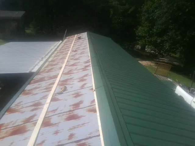 Old rusted panels beside newly installed green metal roofing — Wind Damage Roof Repair by Roofing Brothers in Las Cruces