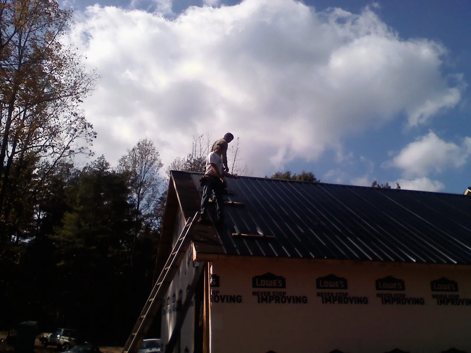 Roofer fastening dark metal panels high against a cloudy sky, from a Roof Inspection job in Las Cruces