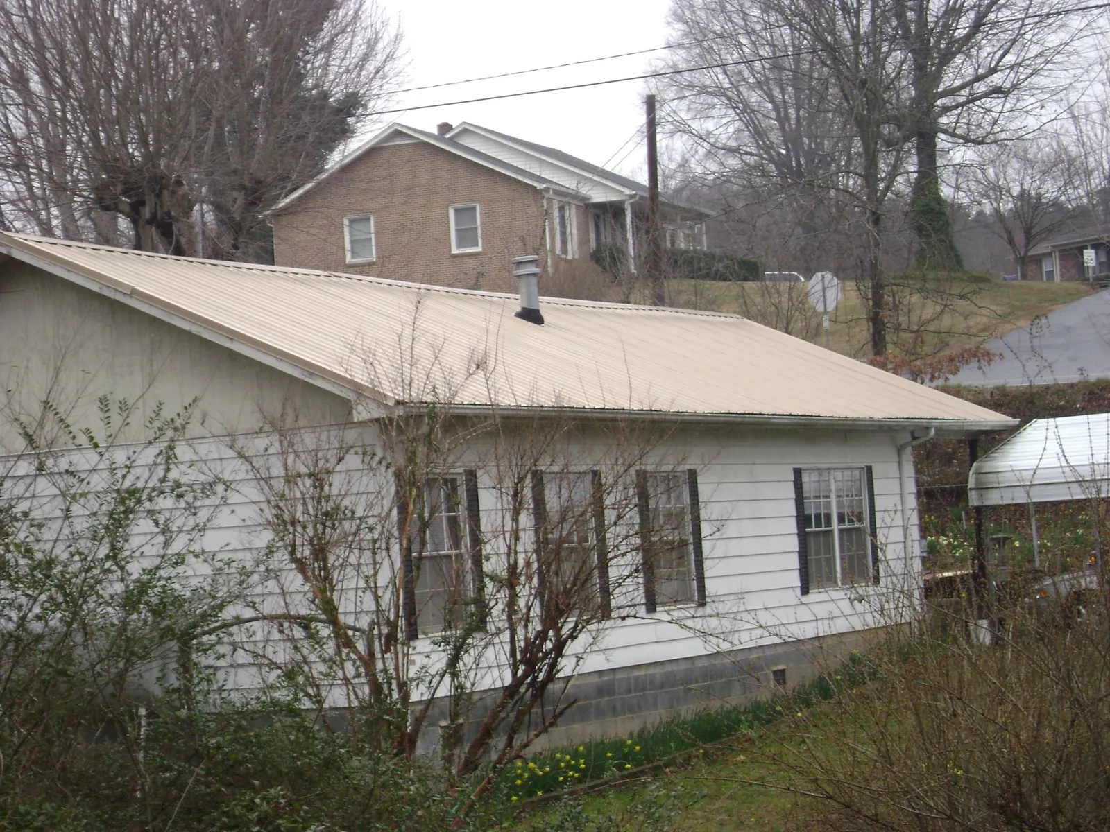 Tan metal roof on a white sided house set into a hillside — Commercial Roofing by Roofing Brothers in Las Cruces